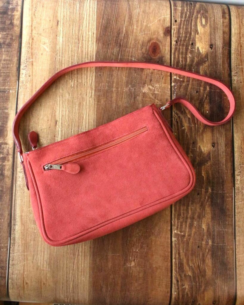 Sac en cuir velours terracotta, porté à l'épaule avec son anse et sa poche extérieure zippée